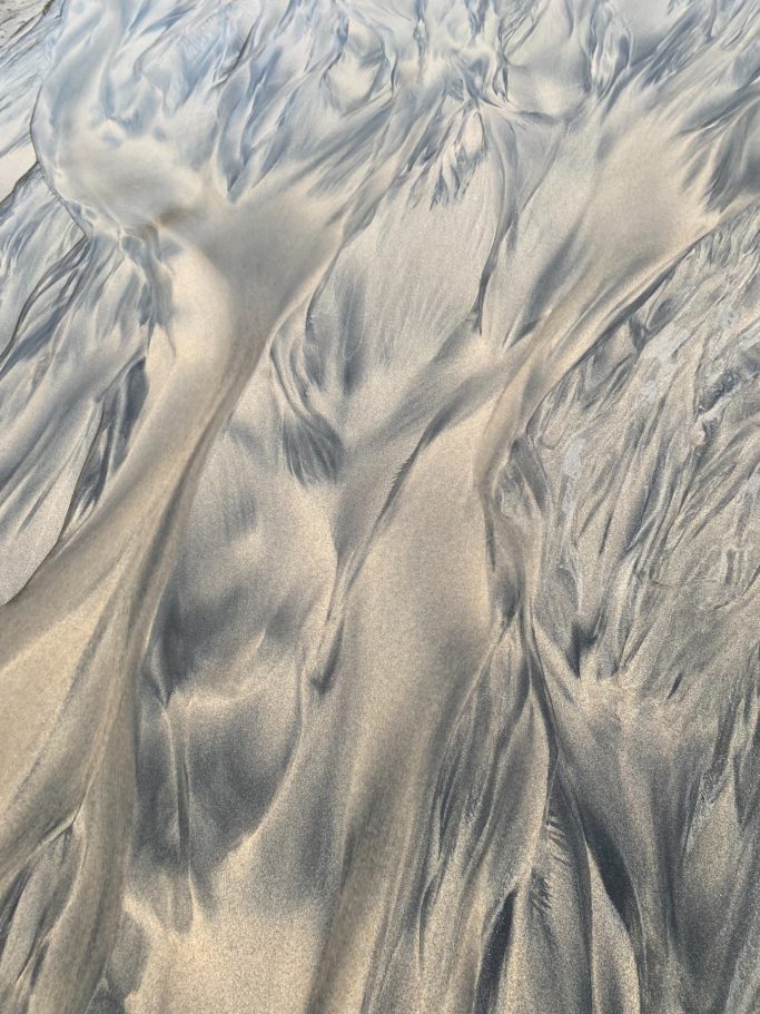 Swirling patterns of sand, creating a textured surface in soft shades of beige and grey.