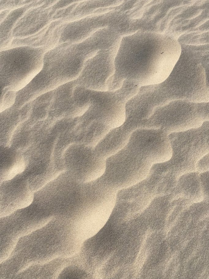 Textured patterns of light and shadows on a sandy surface.